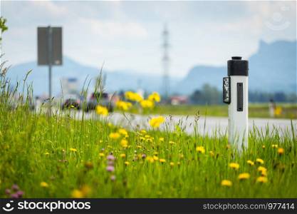 Reflector post at an idyllic asphalted road in summer, flowers and green grass
