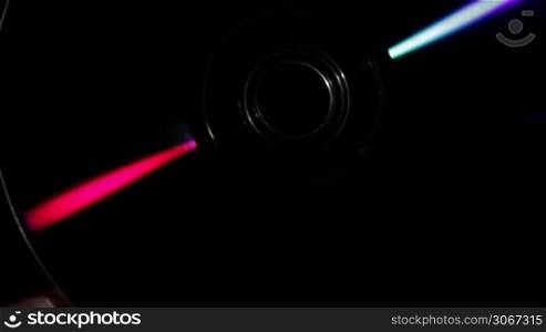Refraction of light. Compact disk rotates in hand on a black background.