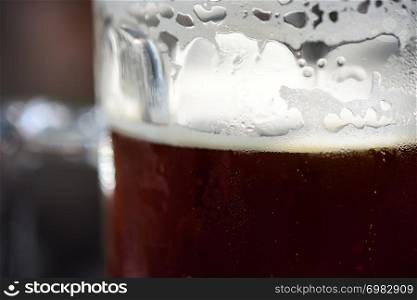Refreshing Cold Pint Of Dark Ale Beer With Condensation, Frothy Foam And Bubbles Ready To Drink