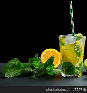 refreshing drink lemonade with lemons, mint leaves, ice cubes and lime in a glass on a black background