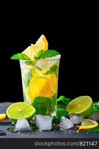 refreshing drink lemonade with lemons, mint leaves, ice cubes and lime in a glass on a black background, copy space