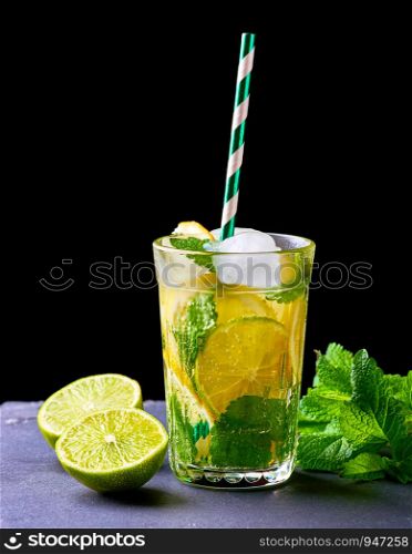 refreshing drink lemonade with lemons, mint leaves, ice cubes and lime in a glass on a black background
