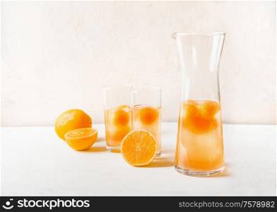 Refreshing lemonade with fruits ice cubes of orange juice in jug and glasses on white table