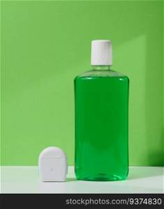 Refreshing mouthwash in a transparent plastic bottle and dental floss on a green background