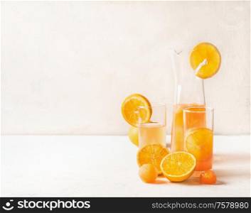 Refreshing orange lemonade with fruits ice cubes of orange juice in jug and glasses on white table