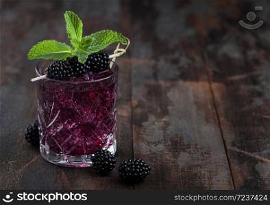 Refreshing summer cocktail with blackberry in crystal glass with ice cubes and mint on wooden background with berries. Space for text