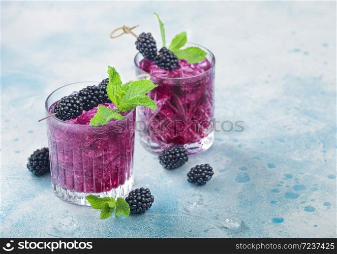 Refreshing summer cocktail with blackberry in crystal glasses with ice cubes and mint on blue background. Soda and alcohol mix. Macro