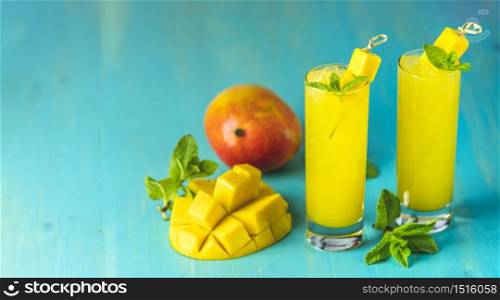 Refreshing summer cocktails made of mango, cold drink or a drink with ice on a blue gray background. Fresh summer ice cold mango cocktail or juice with mint and mango fruit.
