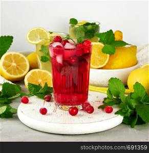 refreshing summer drink of strawberries and cranberries on a white wooden board, behind it are yellow lemons and green mint leaves