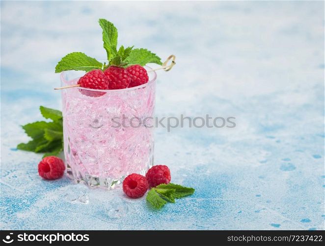 Refreshing summer pink lemonade cocktail in crystal glass with raspberries, ice and mint on light blue background. Space for text