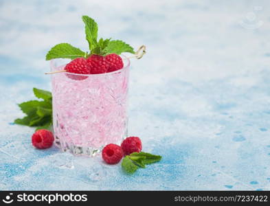 Refreshing summer pink lemonade cocktail in crystal glass with raspberries, ice and mint on light blue background. Space for text