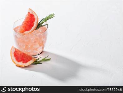 Refreshing summer red grapefruit cocktail in crystal glass with ice, fruit slice and rosemary on white background with deep shadow. Space for text