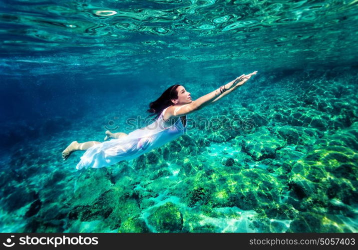 Refreshing swimming underwater, beautiful young woman wearing fashion white long dress and dive into clear transparent sea, luxury summer vacation concept