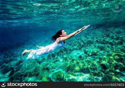 Refreshing swimming underwater, beautiful young woman wearing fashion white long dress and dive into clear transparent sea, luxury summer vacation concept