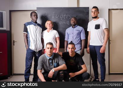 Refugees Welcome: A female German volunteer is proudly posing with young African (Gambia) and Arabic (Algeria and Tunesia) men she is teaching the German language in a refugee camp quickly errected using accomodation containers. Over 1 million refugees arrived in Germany in 2015 alone, integration of these people requires enormous efforts by the government but also by thousands of volunteers providing basic training and services for the refugees.