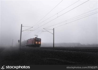 Regional german train traveling through the fog, on a cold day with lights on, near Schwabisch Hall, Germany. Passenger train with a retro locomotive