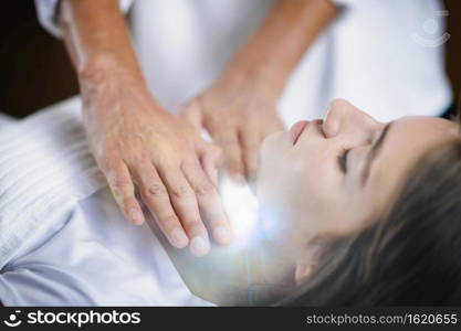 Reiki practitioner standing and healing throat chakra to beautiful teenage girl lying with her eyes closed. Alternative therapy concept.