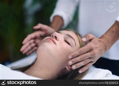 Reiki therapist holding hands on both sides of patient head and transfer energy. Beautiful and peaceful teenage girl lying with her eyes closed. Alternative therapy concept. 