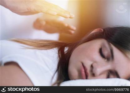 Reiki therapist holding hands over back of the patient and transfer energy. Peaceful teenage girl lying with her eyes closed. Alternative therapy concept of stress reduction and relaxation.  