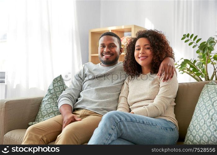 relations and people concept - happy african american couple sitting on sofa and hugging at home. happy african american couple hugging at home