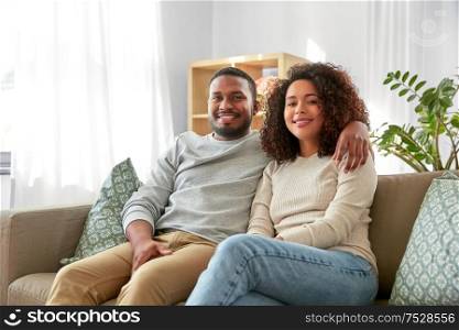 relations and people concept - happy african american couple sitting on sofa and hugging at home. happy african american couple hugging at home