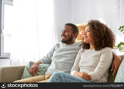 relations and people concept - happy african american couple sitting on sofa and hugging at home. happy african american couple hugging at home