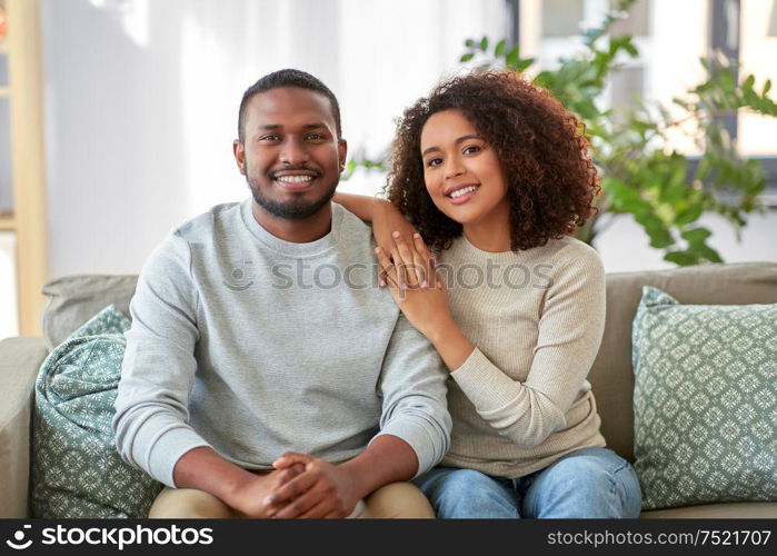 relations and people concept - happy african american couple sitting on sofa at home. happy african american couple on sofa at home