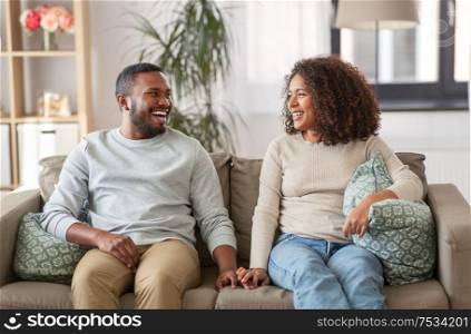 relations and people concept - happy african american couple sitting on sofa at home. happy african american couple on sofa at home