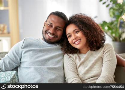 relations and people concept - happy african american couple sitting on sofa at home. happy african american couple on sofa at home