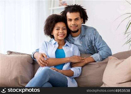relations, communication and people concept - happy couple sitting on sofa and hugging at home. happy couple sitting on sofa and hugging at home