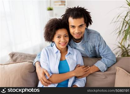 relations, communication and people concept - happy couple sitting on sofa and hugging at home. happy couple sitting on sofa and hugging at home