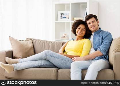 relations, love and people concept - happy smiling international couple resting on sofa at home. happy smiling international couple on sofa at home