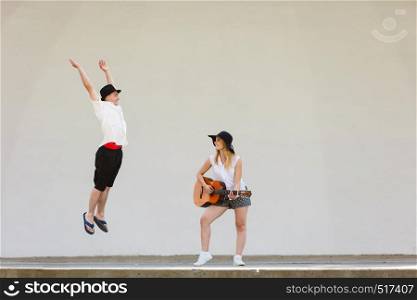 Relationship goals concept. Couple on romantic date. Woman playing guitar, man jumping next to her. Woman playing guitar, man jumping next to her