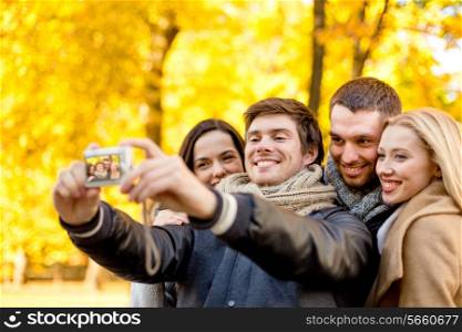relationship, season, friendship, technology and people concept - group of smiling men and women making self portrait with digital camera in autumn park