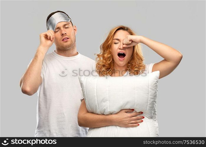 relationships and people concept - couple in white t-shirts with eye sleeping mask and pillow over grey background. couple with eye sleeping mask and pillow