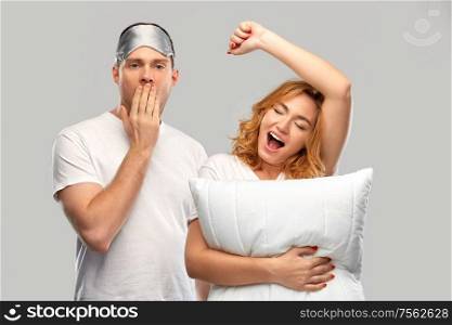 relationships and people concept - couple in white t-shirts with eye sleeping mask and pillow yawning and stretching over grey background. yawning couple with eye sleeping mask and pillow