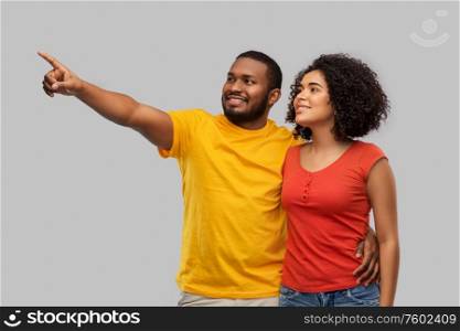 relationships and people concept - happy african american couple pointing finger to something over grey background. happy african american couple