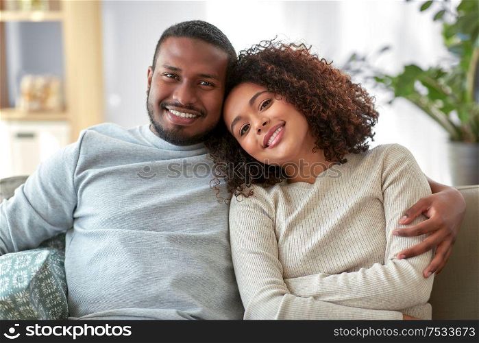 relationships and people concept - happy african american couple sitting on sofa and hugging at home. happy african american couple hugging at home