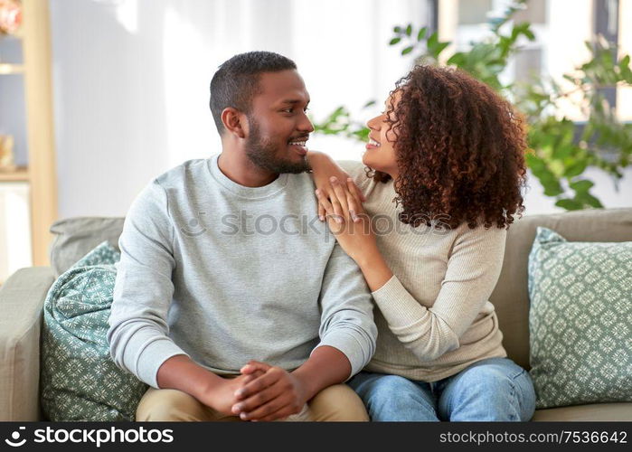 relationships and people concept - happy african american couple sitting on sofa at home. happy african american couple talking at home