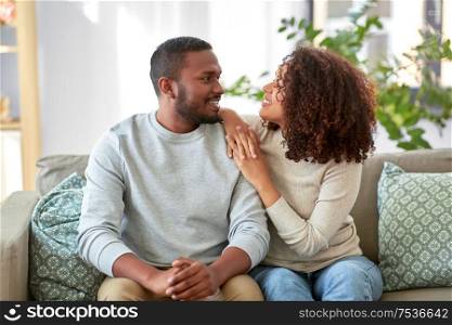 relationships and people concept - happy african american couple sitting on sofa at home. happy african american couple talking at home