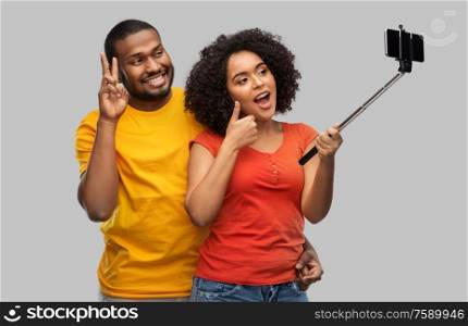 relationships and people concept - happy african american couple taking picture by smartphone on selfie stick over grey background. african american couple taking selfie by cellphone