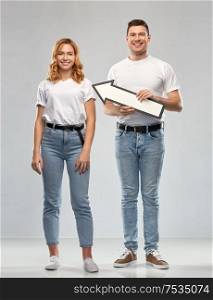 relationships and people concept - happy couple in white t-shirts holding big leftwards thick arrow over grey background. happy couple in white t-shirts with arrow to left