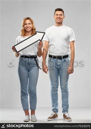 relationships and people concept - happy couple in white t-shirts holding big rightwards thick arrow over grey background. happy couple in white t-shirts with arrow to right