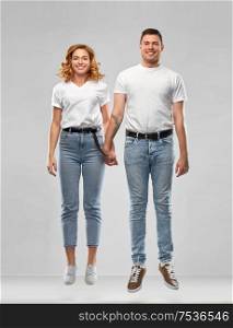 relationships and people concept - happy couple in white t-shirts holding hands and jumping or hanging in air over grey background. happy couple in white t-shirts jumping or hanging