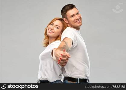 relationships and people concept - happy couple in white t-shirts holding hands over grey background. happy couple in white t-shirts holding hands