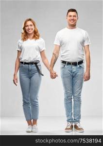 relationships and people concept - happy couple in white t-shirts holding hands over grey background. happy couple in white t-shirts holding hands
