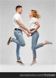 relationships and people concept - happy couple in white t-shirts jumping over grey background. happy couple in white t-shirts jumping