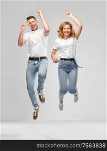 relationships and people concept - happy couple in white t-shirts jumping over grey background. happy couple in white t-shirts jumping