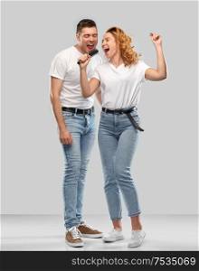 relationships and people concept - happy couple in white t-shirts singing to hairbrush over grey background. happy couple singing to hairbrush