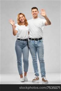 relationships and people concept - happy couple in white t-shirts waving hands over grey background. happy couple in white t-shirts waving hands